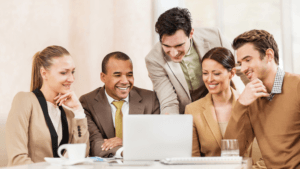 A group of individuals, 4 sitting, 1 standing, lean in towards a laptop with a website for nonprofits.